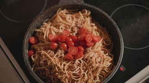 Top-down cooked spaghetti with cherry tomatoes in frying pan, glossy sauce, warm Stock Footage 346658027