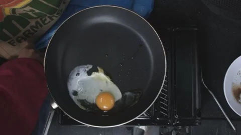 Top down of cracking an egg onto a camping stove Stock Footage 266653790