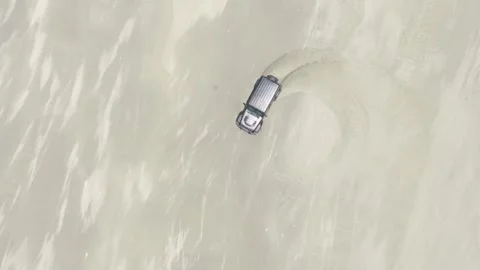 Top down drone ascent of 4x4 doing donuts on beach sand circular drift pattern Stock Footage 333987840