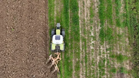 Top down drone close up shows tractor with plow turning green field into rough Stock Footage 311907225