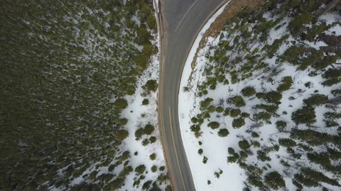 Top down drone shot of a curving mountain road with snowy trees on either side Stock Footage 167676456