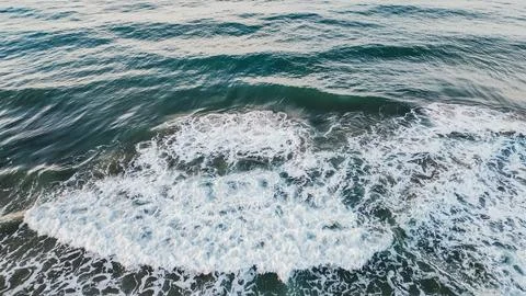 Top down drone shot of deep teal ocean water with white foamy wave spreadin.. Stock Photos