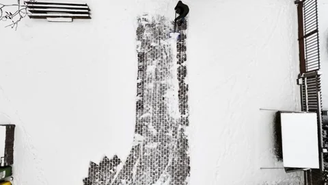 Top-down drone shot of a man clearing a cobblestone walkway with a shovel Stock Footage 328358559