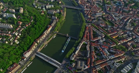 Top down drone shot over town at sunset along a blue river. A tourist ship moves Stock Footage 274133672