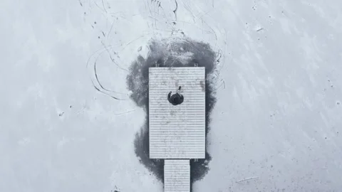 Top down drone shot of person walking along a boardwalk towards a frozen lake Stock Footage 146294475
