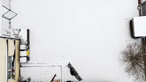 Top-down drone shot as a resident begins clearing fresh snow with a blue Video stock 328636316