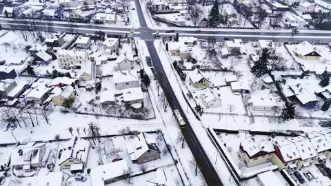 Top-down drone shot of a snowy suburban intersection with crosswalks, cars, and Stock Footage 328871564