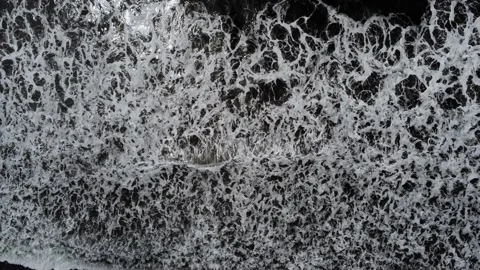 Top down drone shot, waves rush up black sand beach shore Stock Footage 137649613