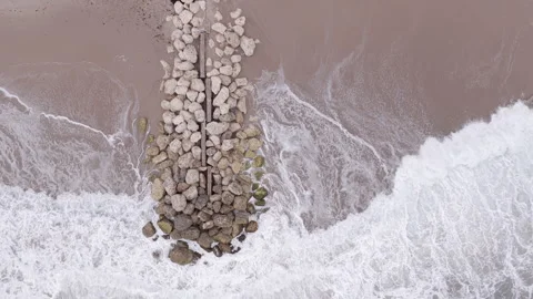 Top down drone shot of waves crashing against rocky beach jetty Stock Footage 334810232