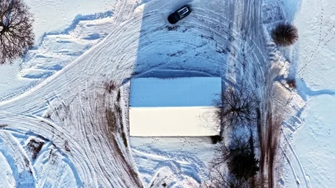 Top-down drone view of a car drifting donuts on an icy snowy field near a farm Stock Footage 327837361