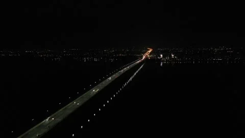 Top-down drone view of cars driving across a long illuminated bridge at night 库存影片 342772019