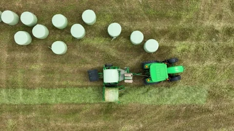 Top down drone view of green tractor in farm land wrapping hay bales in plastic Stock Footage 292987177