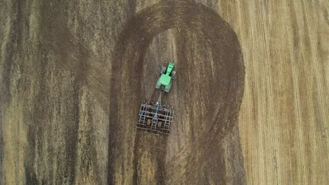 Top-down drone view of a green tractor pulling a cultivator across a tilled Stock Footage 324832235