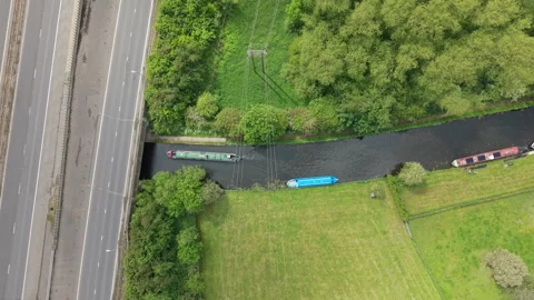 Top-Down Drone View of Narrowboat Passing Under Motorway Bridge Canal in England Stock-Footage 335114427