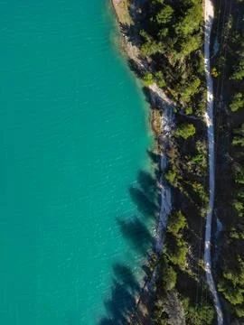 Top down drone view of turquoise water reservoir, footpath surrounded by trees Stock Photos