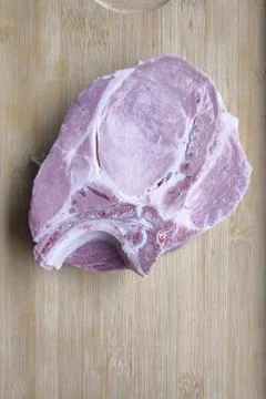 A top-down, flat lay photograph of a single raw, bone-in pork chop resting on Stock Photos
