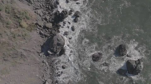 Top-down forward tracking of wave on rocks along hillside Stock Footage 336793268