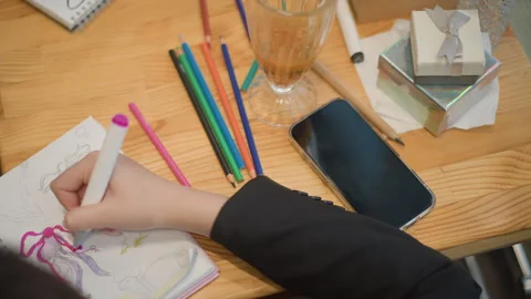 Top down hand sketching and erasing in spiral sketchbook on wooden desk with Stock Footage 347542549