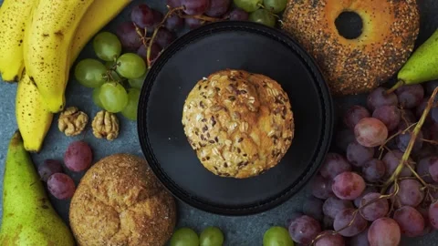 Top down loop of bun on brown plate with grapes bananas pears and bagel Video stock 320029504