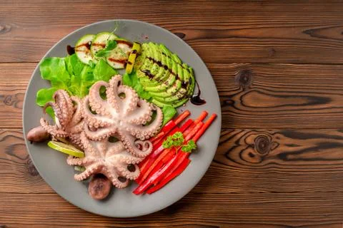Top down of octopus served with sliced avocado, lettuce, red pepper, lime, cu Stock Photos