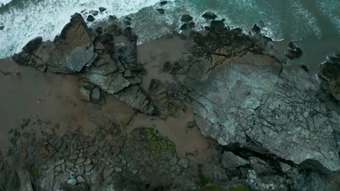 A top down, overhead aerial of waves crashing on rocks and a reveal of surfers Stock Footage 137421737