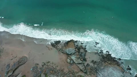 A top down, overhead aerial of waves crashing on rocks and a reveal of surfers Stock Footage 137421859