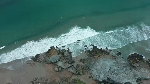 A top down, overhead aerial of waves crashing on rocks and a reveal of surfers Stock Footage 137422150