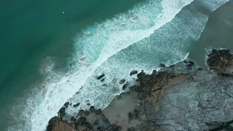 A top down, overhead aerial of waves crashing on rocks and a reveal of surfers Stock Footage 137422178