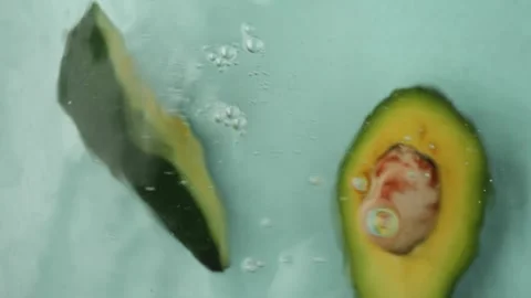 From a top-down perspective, an avacado half descends gracefully into water Vidéo 270002099