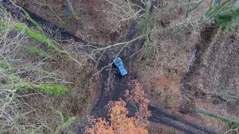 Top-down perspective of a car driving along a bumpy, muddy path in a bare f.. 스톡 동영상 259158674