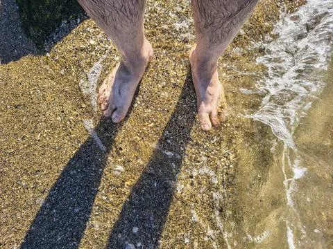 Top-down perspectives of human bare feet standing on wet sand and multiple fo Stock Photos