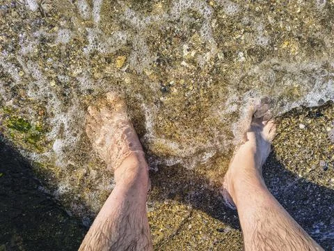 Top-down perspectives of human bare feet standing on wet sand and multiple fo Stock Photos