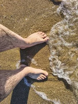 Top-down perspectives of human bare feet standing on wet sand and multiple fo Stock Photos