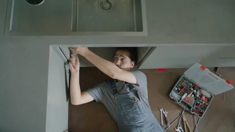 Top Down of Plumber Lying on Kitchen Floor, Repairing Sink Pipe Stock Footage 337007712