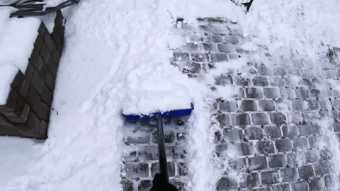 Top-down POV pushing a snow shovel along a cobblestone driveway, clearing a Video stock 329488876