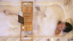 Beautiful girl in a bathtub with candles in glasses on the floor and fluffy  feathers on a white table. Stock Video Footage by ©petrunine #325087296