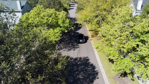 Top-down rear aerial drone shot of a Tesla car driving along a suburban street 库存影片 321116979
