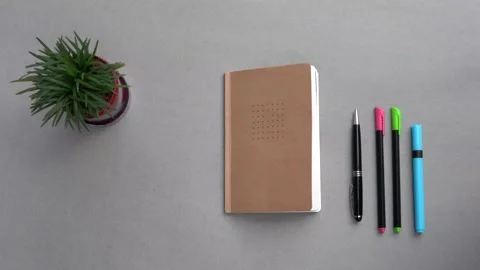 Top down shot of a closed notebook, pens and a plant Stock Footage 147405511