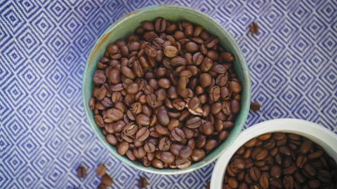 Top down shot of coffee beans sprinkled into a bowl full of beans in slow motion Stock Footage 130587019