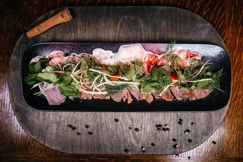 Top-down shot of an elegantly arranged fish carpaccio on a rectangular black  Foto stock