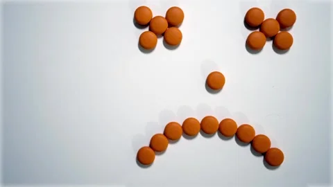 Top down shot of medical orange pills in a shape of unhappy face icon Stock Footage 337150404