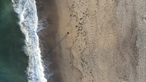 Top down shot of a person walking along the shorelie of a beach in Australia Stock Footage 250070941