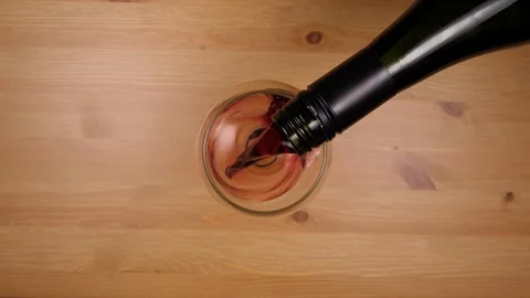 Top down shot of red wine being poured into glass on wood table. Stock Footage 86536666