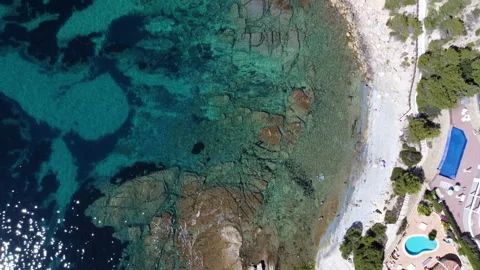 Top down shot of transparent blue water rock beach next to houses and trees. Stock-Footage 258302027
