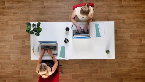 Top down shot, two hard-working females typying on their laptops and sitting at Video stock 96579353