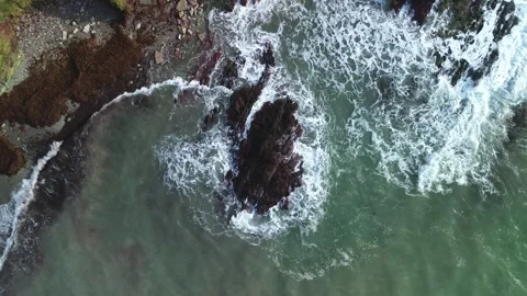 Top-down shot of waves crashing on rocky coastline with slow rotating ascent Stock Footage 328477317