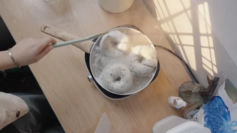 Top down slow motion view of a person boiling three raw homemade bagels with Stock Footage 328983534