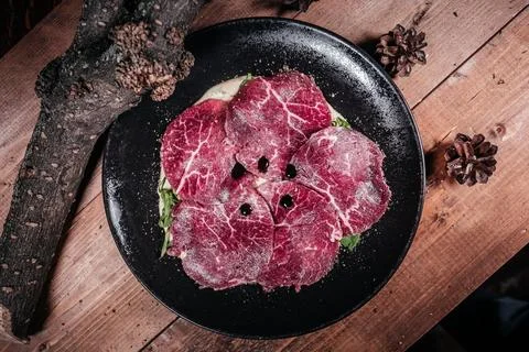 Top-down studio shot of thinly sliced beef carpaccio artfully arranged on a b Stock Photos