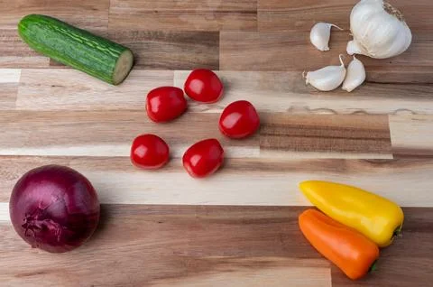 Top-down view of assorted fresh vegetables arranged on a striped wooden cutti Stock Photos