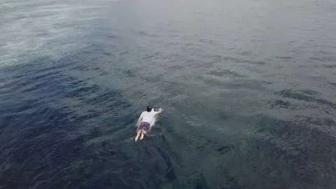 Top down view back of a male surfer paddling in ocean on his surfboard. Video stock 131537027